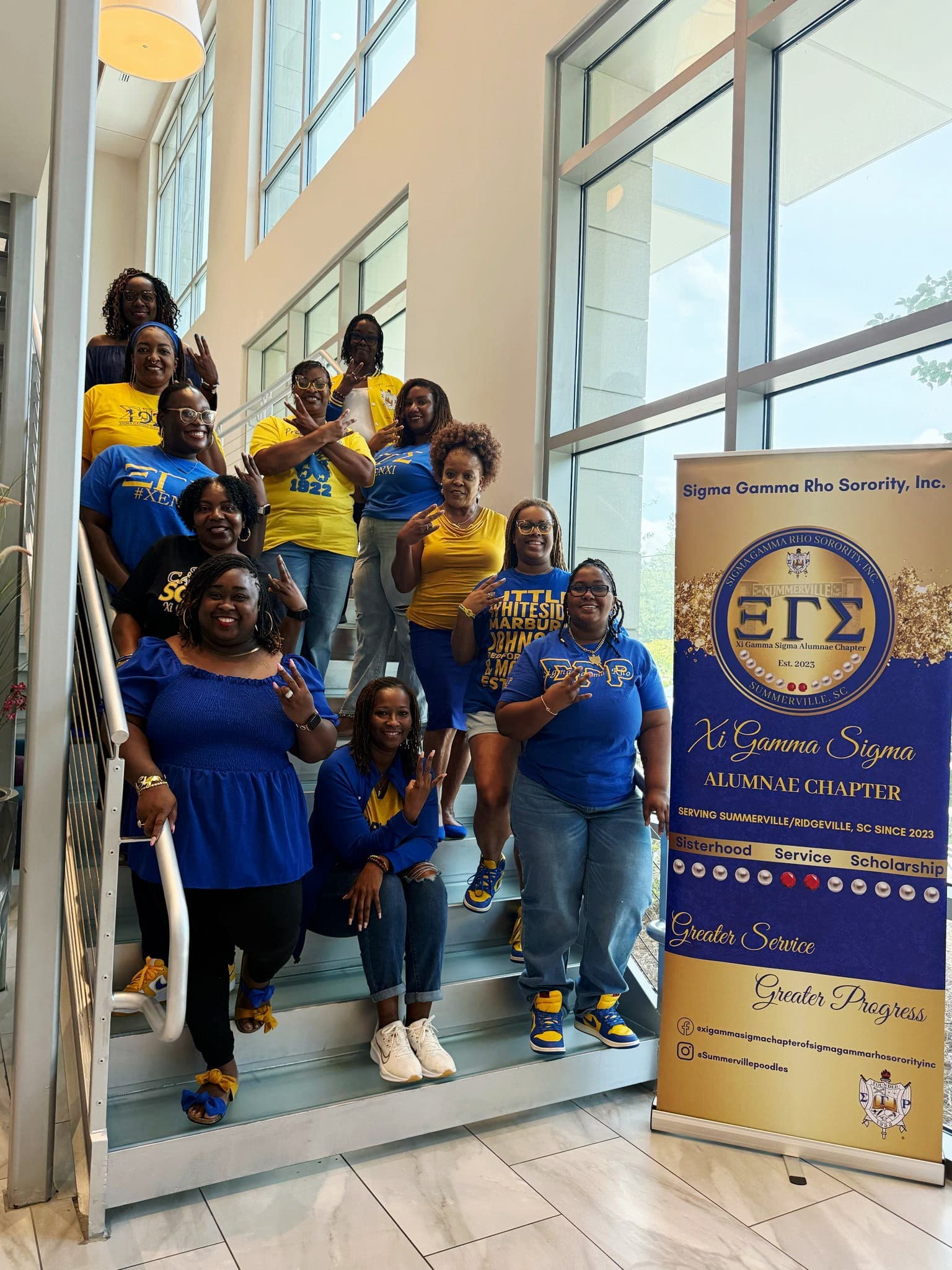 Xi Gamma Sigma sorors gathered on a staircase with the chapter banner